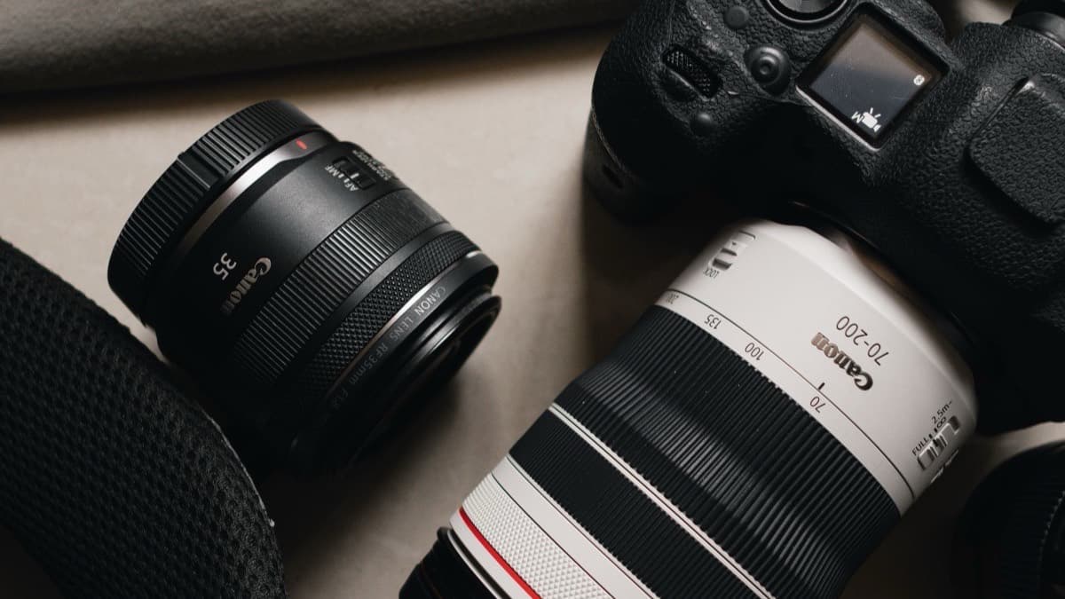 A Canon 35mm prime lens standing beside a white Canon 70-200 zoom lens attached to a camera body, their markings legible.