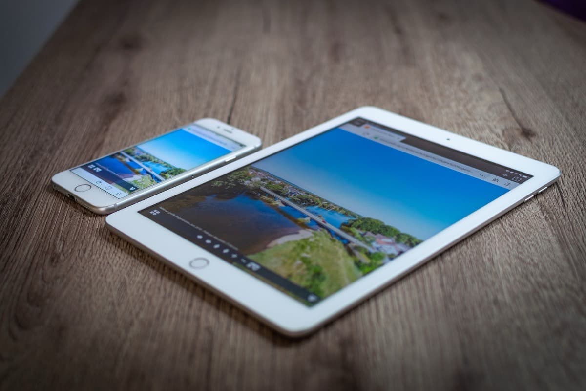An older iPad and an iPhone lying together on a wooden table with their screens switched on.
